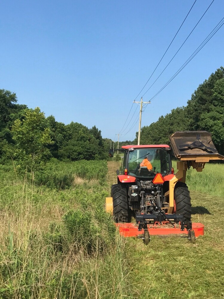 Orange Bclean Brush Hog trimming a large field of tall grass